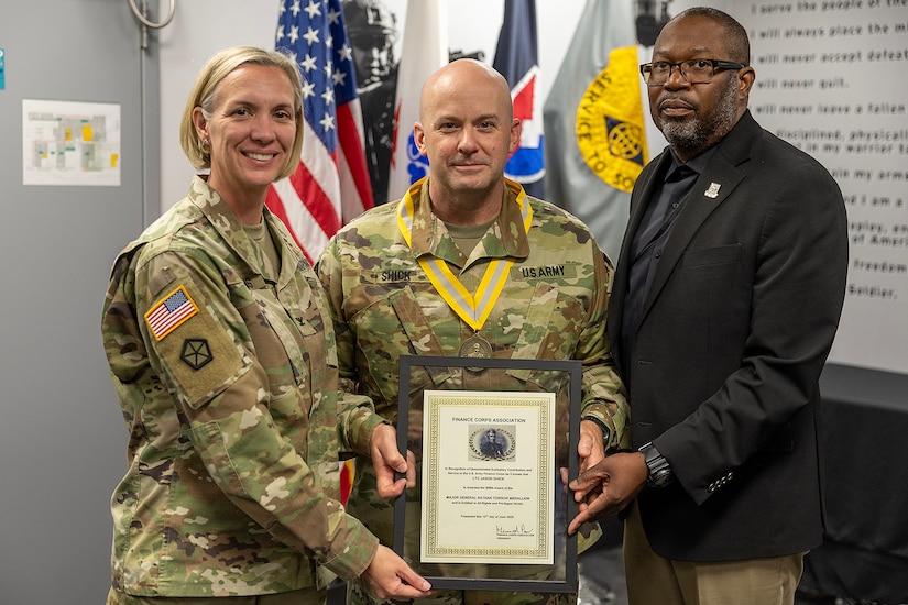Col. Michelle M. Williams, U.S. Army Financial Management Command commander, left, and Gennaro Penn, U.S. Army Finance Corps Association president, right, present a Maj. Gen. Nathan Towson Regimental Medallion to Lt. Col. Jason L. Shick, USAFMCOM plans and operations officer, at the Maj. Gen. Emmett J. Bean Federal Center in Indianapolis June 2, 2025. The Towson was established by the U.S. Army Finance Corps Association on May 7, 1993, to recognize exceptional achievement or exemplary service by currently serving U.S. Army finance and comptroller commissioned officers, non-commissioned officers, enlisted Soldiers and civilians demonstrating exceptional leadership and whose accomplishments clearly distinguish them from their peers. (U.S. Army photo by Mark R. W. Orders-Woempner)