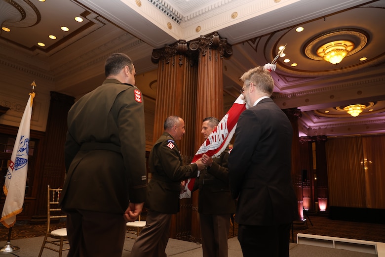 Photo shows a military officer handing a flag representing the unit colors to another military officer during a Change of Command ceremony.