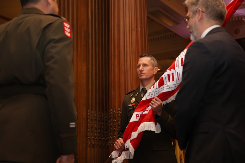 Photo shows a military officer accepting a flag representing the unit colors during a ceremony.