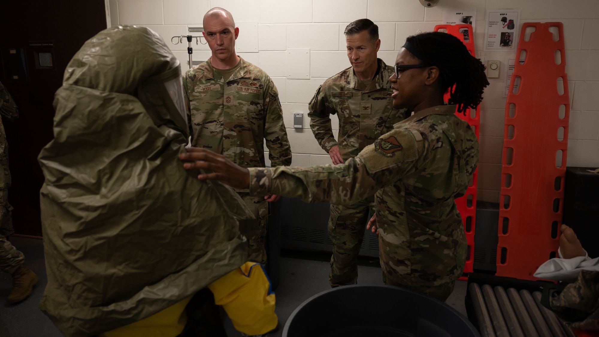 U.S. Air Force Senior Airman Terra Thomas, right, 51st Operational Medical Readiness Squadron dental assistant, briefs Col. Ryan Ley, center right, 51st Fighter Wing commander, and Chief Master Sgt. Carl Vogel, center left, 51st FW command chief, at Osan Air Base, Republic of Korea, July 15, 2025. Coveralls are a protective suit worn by medical personnel in the event if a patient has any chemical exposure and needs to be decontaminated before any treatment is received to prevent further contamination. (U.S. Air Force photo by Senior Airman Rome Bowermaster)