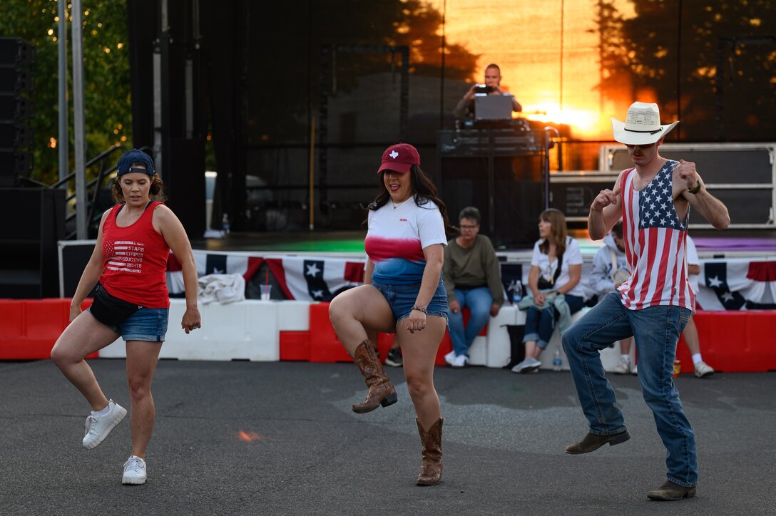 Three people line dance in front a stage.