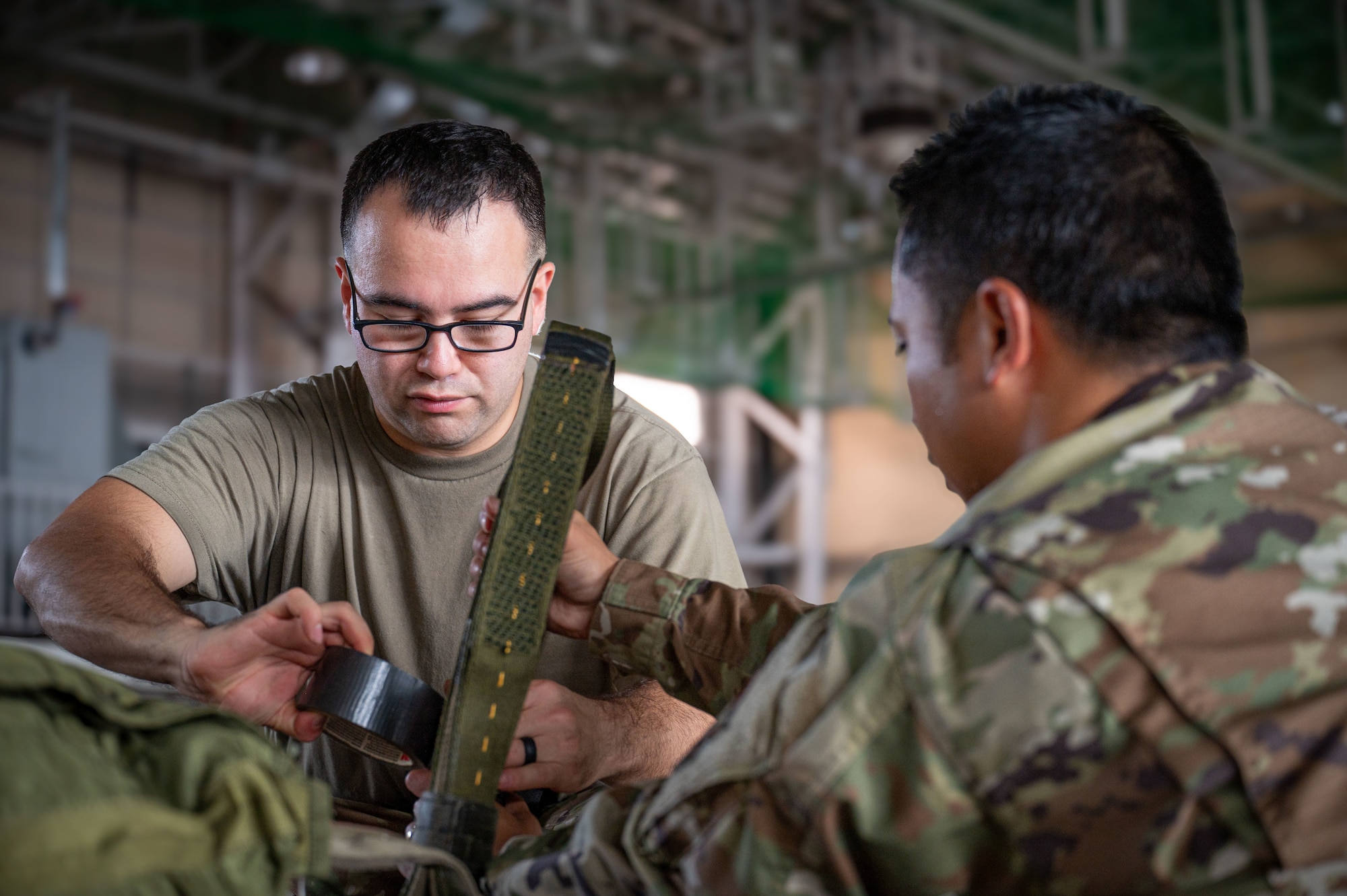 Two military members tighten a strap on a cargo bundle.