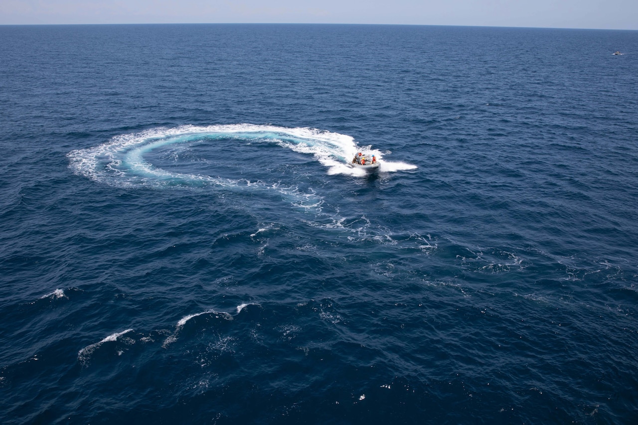Sailors and Marines operate an inflatable boat in the ocean under a blue sky.