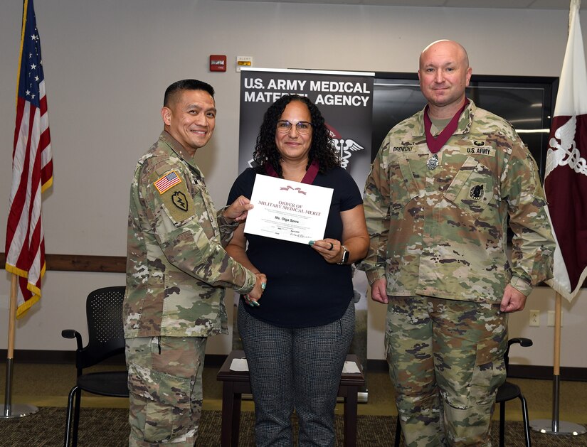 Liz Serra shakes hands with Col. Joselito “Joe” Lim, commander of the U.S. Army Medical Materiel Agency, following her induction into the Order of Military Medical Merit during a quarterly town hall July 10 at Fort Detrick, Maryland. Also pictured is USAMMA Sgt. Maj. Todd Brenecki. Serra, a 15-year Army veteran, has served in USAMMA’s Distribution Operations Center (DOC) for nearly a decade and led the DOC’s vaccine distribution efforts during the COVID-19 pandemic response.