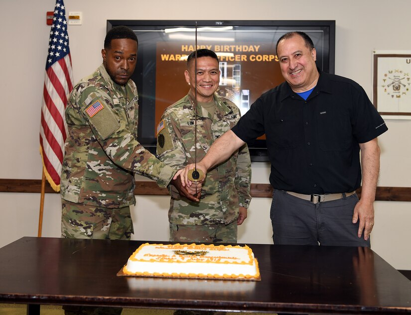 U.S. Army medical logistics leaders gathered July 9 for a cake-cutting ceremony to recognize the 107th birthday of the Army Warrant Officer Corps. Pictured, from left, preparing to cut the cake are Chief Warrant Officer 3 Garron Johnson, medical equipment readiness officer, Army Medical Logistics Command; Col. Joselito “Joe” Lim, commander, U.S. Army Medical Materiel Agency, and Wilmer Tapia, retired chief warrant officer two and current Army Civilian in USAMMA’s Medical Maintenance Management Directorate.