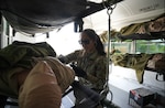 Woman in uniform checks the blood pressure of a simulated casualty aboard an ambulance.