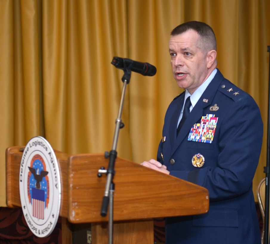 Maj. Gen. David Sanford in dress uniform speaks from behind a podium with the DLA emblem
