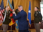 Maj. Gen. David Sanford passes a flag with the unit colors to U.S. Army Col. Tracy Yates, with Col. Adrian J. Sullivan looking on in the background