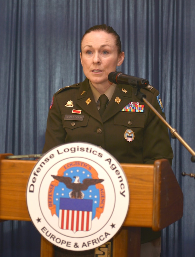 Col. Adrian J. Sullivan speaks in dress uniform behind a podium with the Defense Logistics Agency emblem