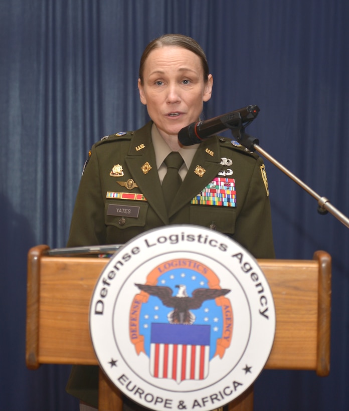 Col. Tracy Yates speaks in dress uniform behind a podium with the Defense Logistics Agency emblem