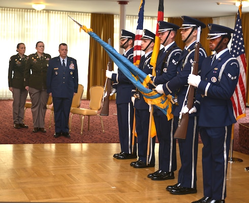 A color guard stands at attention with flags, and the official party is standing in the background