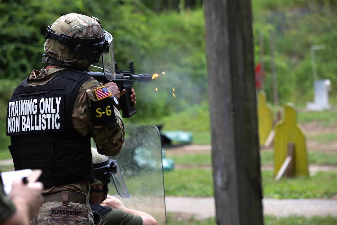 A National Guard soldier fires a service weapon at a target, as seen from behind.