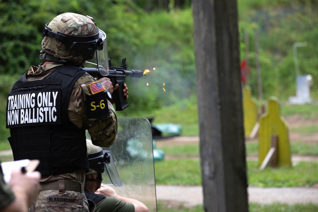 A National Guard soldier fires a service weapon at a target, as seen from behind.