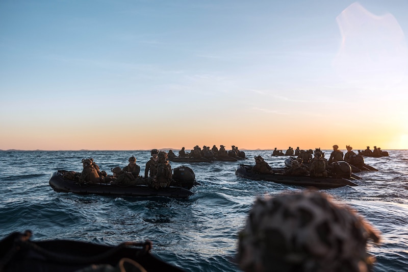 Marines ride small boats on ocean water during lowlight conditions.