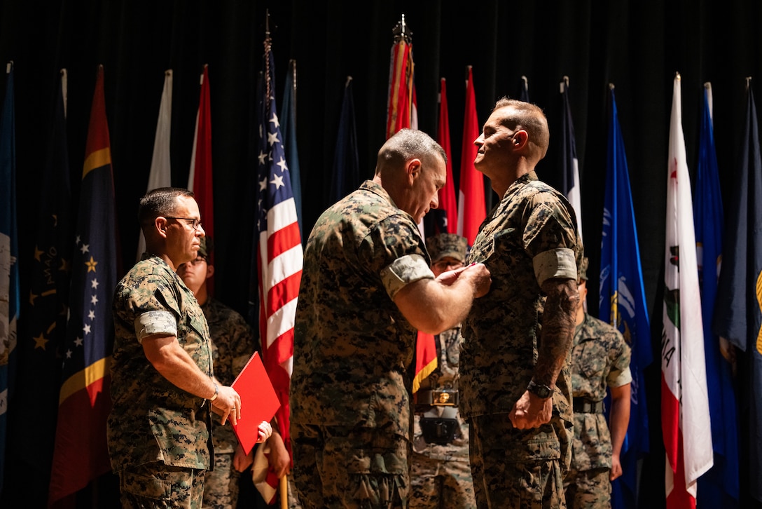 U.S. Marine Corps Brig. Gen. Ralph J. Rizzo Jr., center left, commanding general, Marine Corps Installations East-Marine Corps Base Camp Lejeune, pins a Legion of Merit medal on Col. Garth W. Burnett, outgoing commanding officer, Marine Corps Air Station (MCAS) New River, during a change of command ceremony at MCAS New River in Jacksonville, North Carolina, July 17, 2025. The ceremony represented the transfer of responsibility, authority and accountability from the outgoing to the incoming commanding officer. (U.S. Marine Corps photo by Cpl. Loriann Dauscher)
