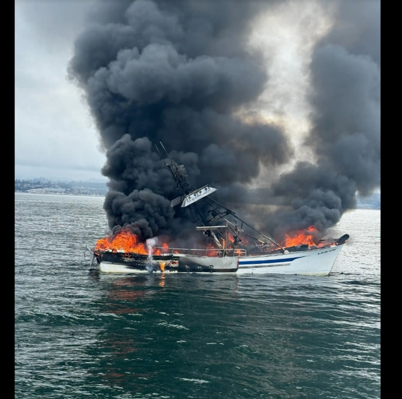 A boat is seen on fire and billowing smoke on the water.