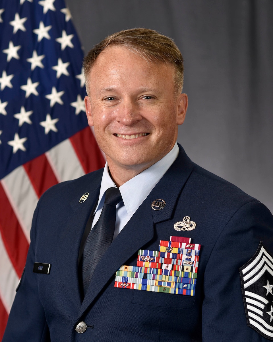 military member poses in front of a flag while wearing the Air Forces dress blues