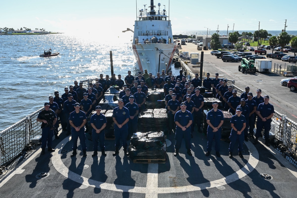 The crew of USCGC Resolute (WMEC 620) pose for a group photo during a drug offload at Coast Guard Sector St. Petersburg, July 17, 2025. Resolute deployed in support of Joint Interagency Task Force-South (JIATF-South), an interagency and international task force that conducts counter-illicit trafficking and security cooperation operations in the Caribbean Sea and Atlantic and Pacific Oceans. (U.S. Coast Guard photo by Petty Officer 1st Class Riley Perkofski)