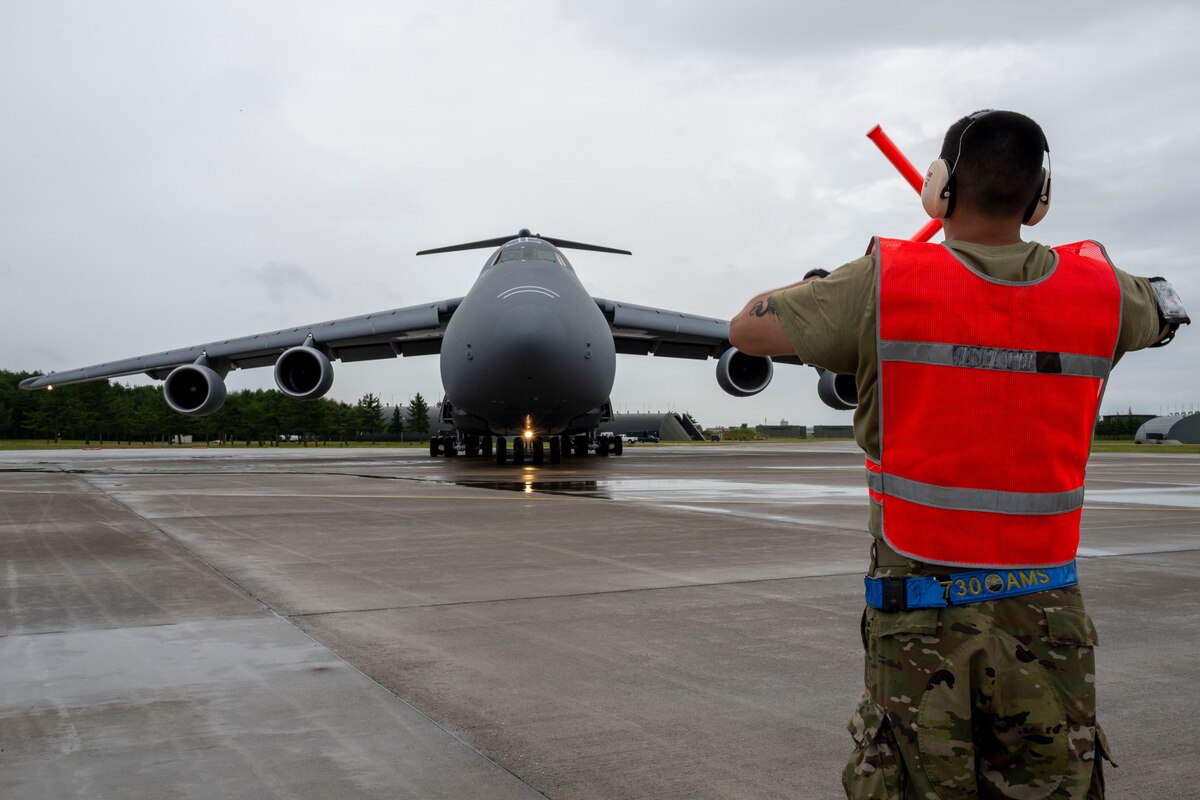 A U.S. Air Force Airman assigned to the 730th Air Mobility Squadron signals a U.S. Air Force C-5M Super Galaxy aircraft to stop during exercise Resolute Force Pacific (REFORPAC) 2025 at Misawa Air Base, Japan, July 16, 2025.