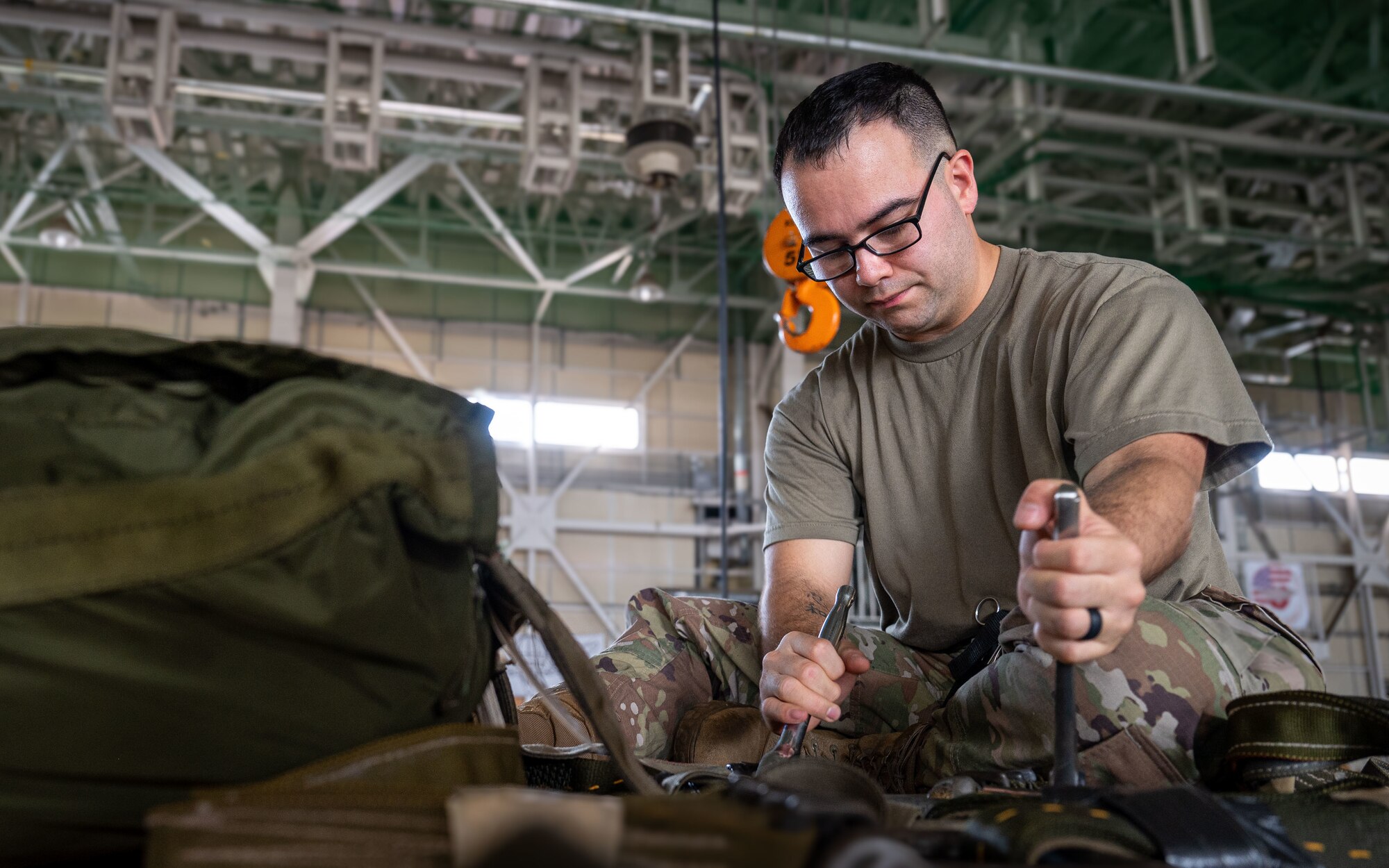 A military member tightens a strap on a cargo bundle.