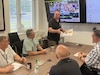 John Schulz (center) briefs some of his fellow staff members from Army Field Support Battalion-Germany at the battalion conference room in Vilseck, Germany, July 18, 2025. Schulz is a transportation specialist at AFSBn-Germany in support operations. He’s also a State of California National Guardsman and a lieutenant colonel who, in addition to this, served for 20 years in the active Army and 16 years in the U.S. Army Reserve. (U.S. Army courtesy photo)