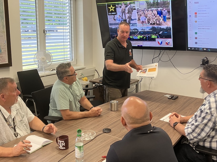 John Schulz (center) briefs some of his fellow staff members from Army Field Support Battalion-Germany at the battalion conference room in Vilseck, Germany, July 18, 2025. Schulz is a transportation specialist at AFSBn-Germany in support operations. He’s also a State of California National Guardsman and a lieutenant colonel who, in addition to this, served for 20 years in the active Army and 16 years in the U.S. Army Reserve. (U.S. Army courtesy photo)