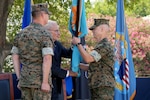 A man in a camouflage military uniform takes a blue flag from a man in a blue suit. There is another man in a camouflage military uniform standing to the left of them.