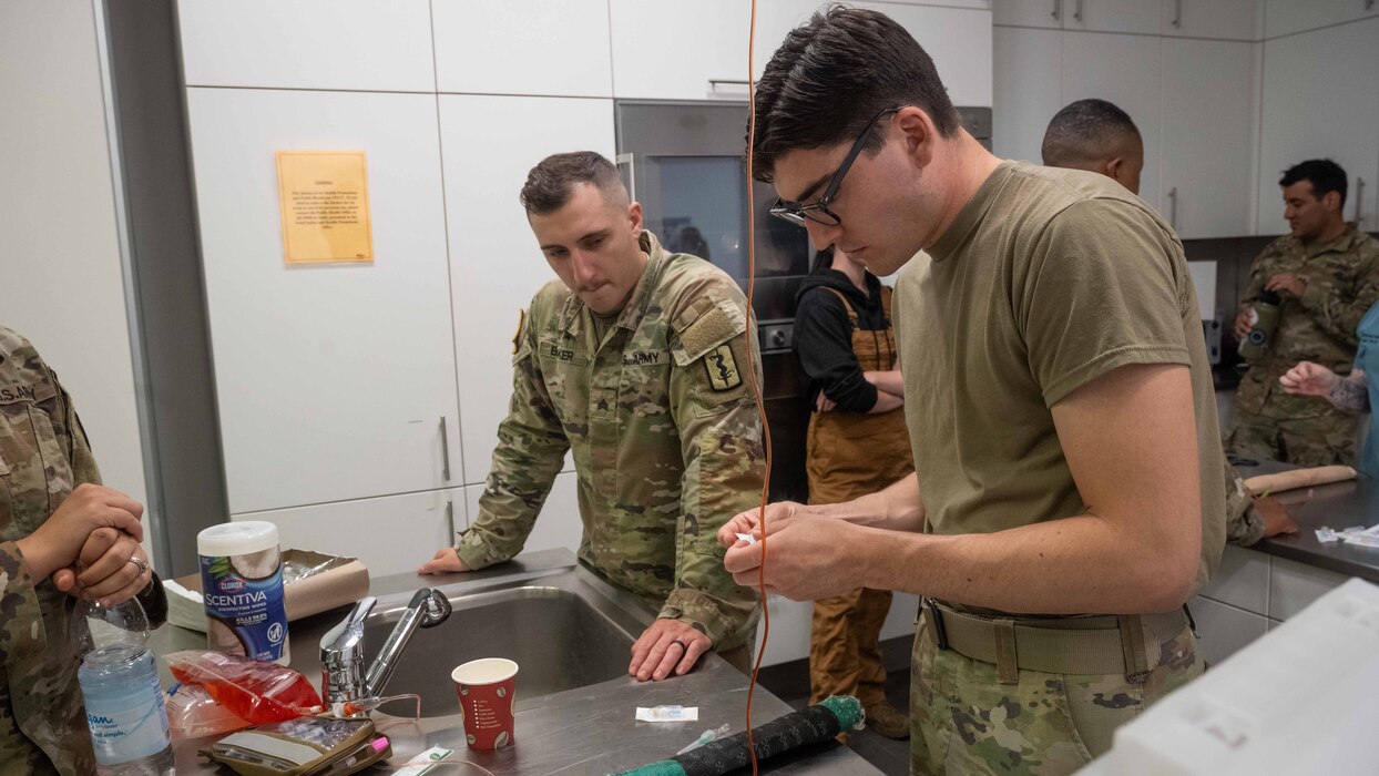 U.S. Army Sgt. Anthony Becker, 30th Medical Brigade animal care specialist, left, and U.S. Air Force Airman 1st Class Matthew Clifford, right, 52nd Operational Medical Readiness Squadron medical technician, practice treating a simulated injured dog leg during canine Tactical Combat Casualty Care simulation training at Spangdahlem Air Base, Germany, July 16, 2025. Airmen strengthen their medical readiness through cTCCC training, ensuring they are prepared to provide life-saving care to military working dogs injured in the line of duty. (U.S. Air Force photo by Senior Airman Darius Frazier)
