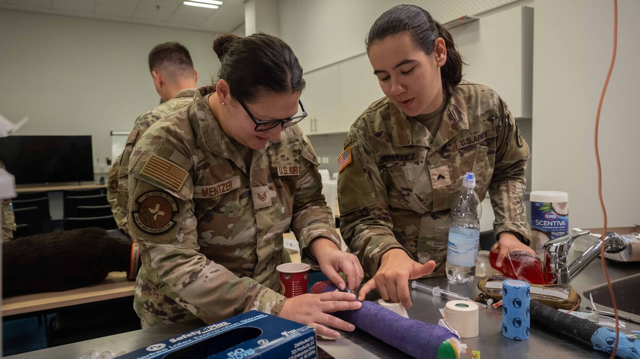 U.S. Air Force Staff Sgt. Collene Mentzer, left, 52nd Medical Group medical technician, and U.S. Army Cpl. Syarra Bermudez, Public Health Command Europe animal care specialist, practice treating a simulated injured dog leg during canine Tactical Combat Casualty Care simulation training at Spangdahlem Air Base, Germany, July 16, 2025. U.S. Army instructors led the training, strengthening joint force readiness and ensuring both services are prepared to care for K-9 partners in combat environments. (U.S. Air Force photo by Senior Airman Darius Frazier)