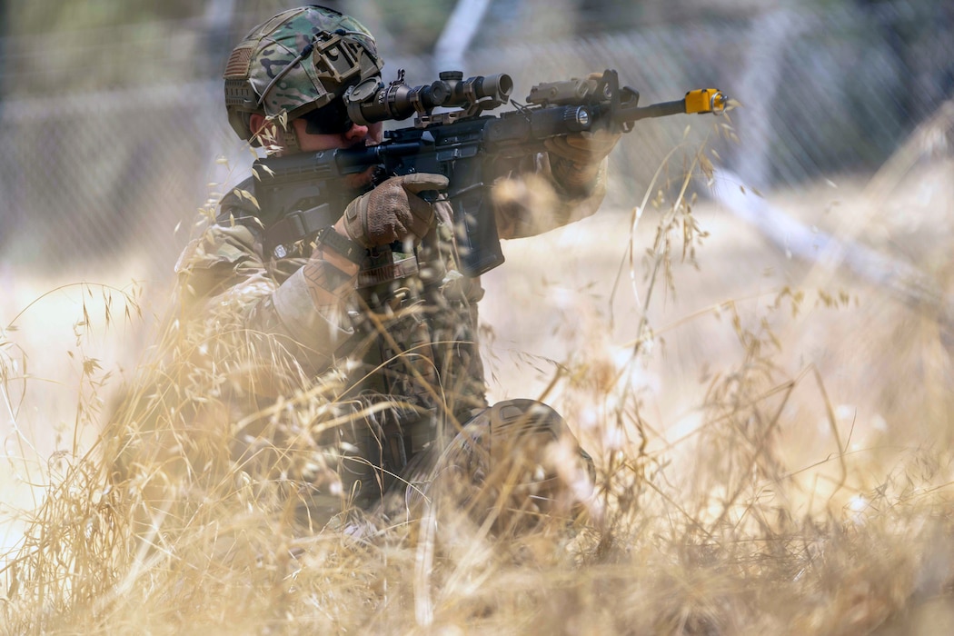 Airman in tall grass aiming rifle