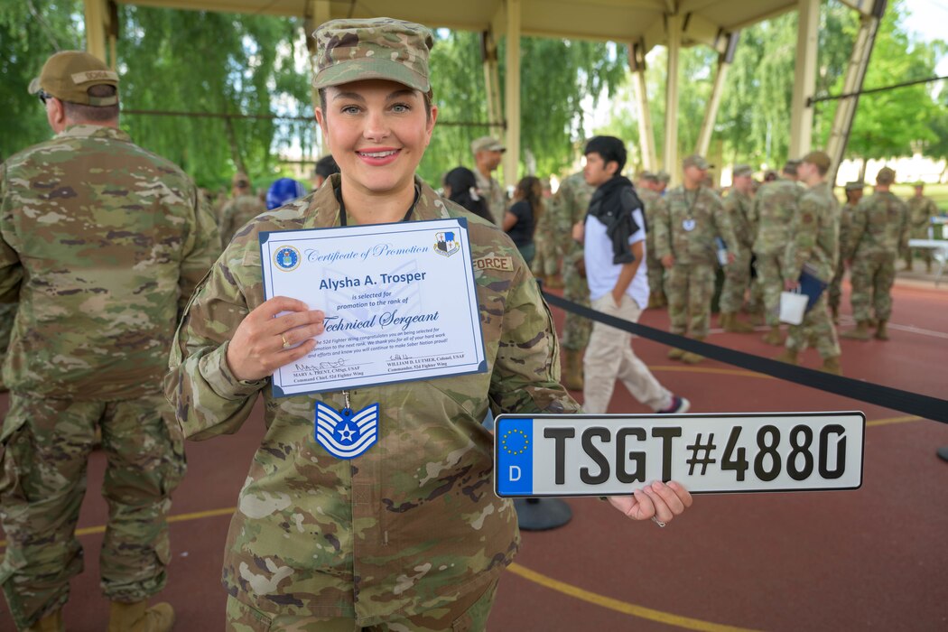 A service member poses with a plaque and a certificate.
