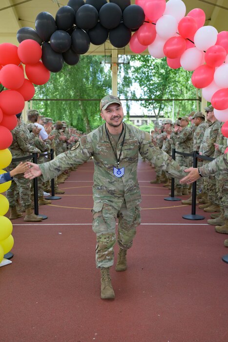 A person walking under a balloon arch receives a high five from each side of the aisle.