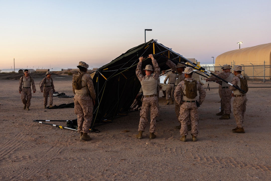 A group of Marines set up a tent outside in desert terrain during lowlight.