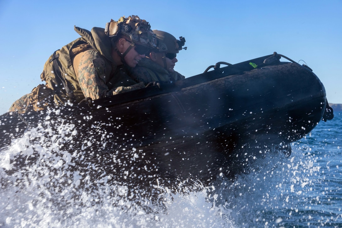Two Marines sail at sea on a small craft as water splashes around them.