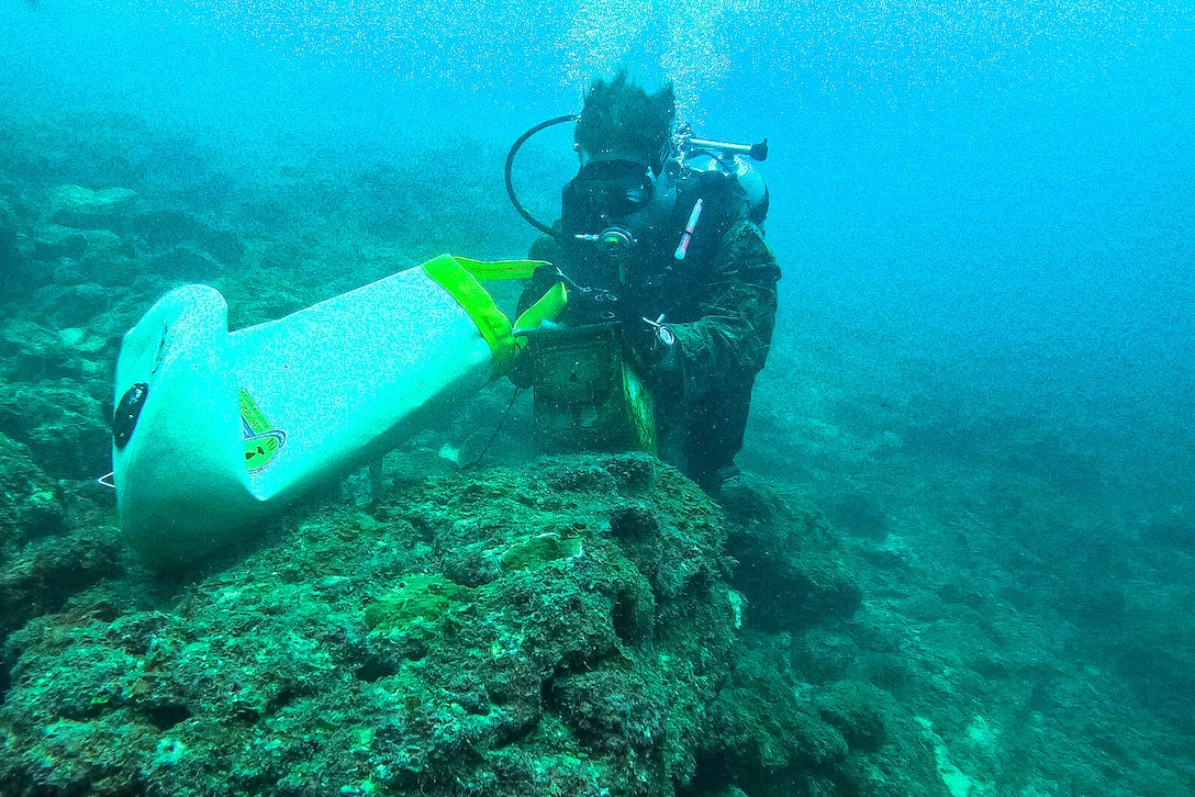 A Marine in dive gear moves a piece of equipment on the ocean floor.