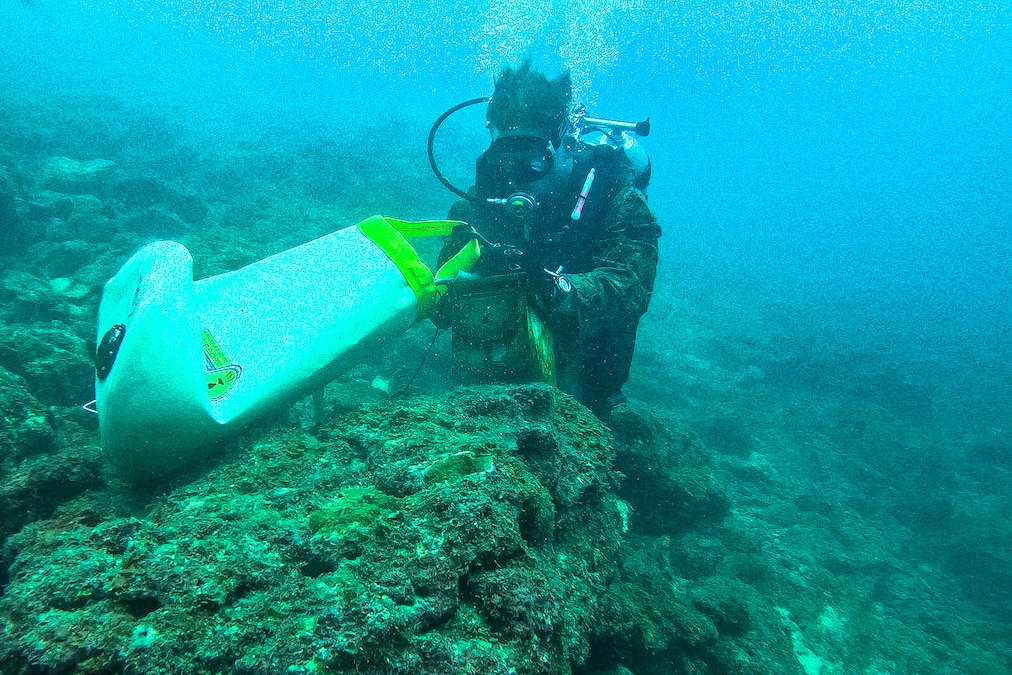 A Marine in dive gear moves a piece of equipment on the ocean floor.