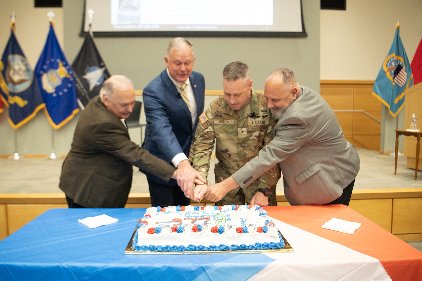 three civilian men and one uniformed man cut a cake together