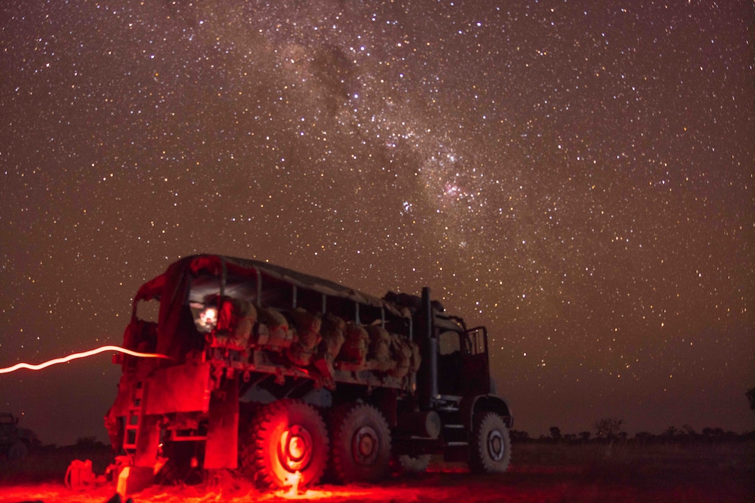 A military vehicle surrounded by red light is parked under stars in a night sky.