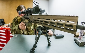 A combat arms training and maintenance instructor examines the scope on an M110A! rifle.