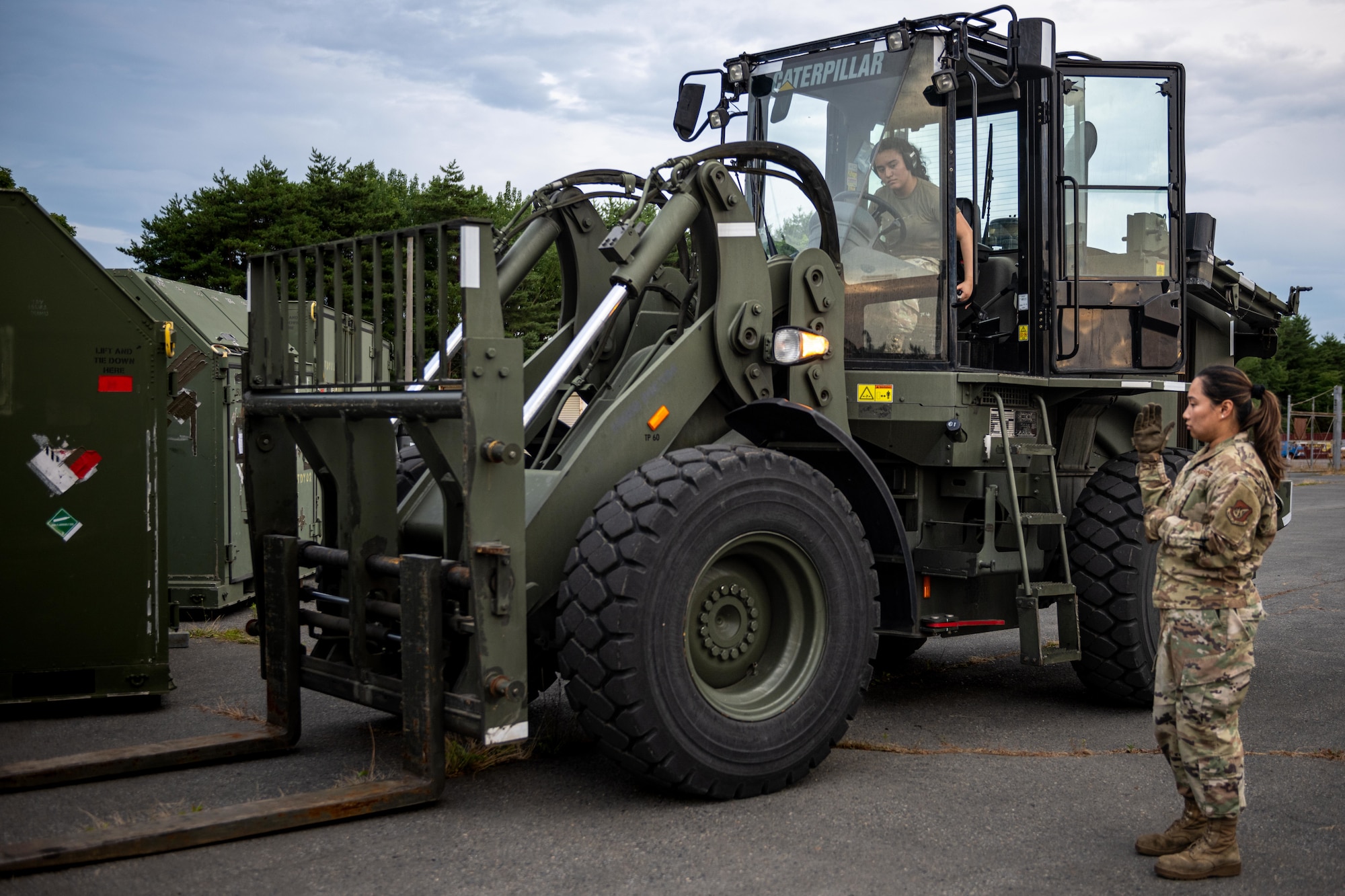 U.S. Air Force Staff Sgt. Sheila Tapinit, right, 35th Logistic Readiness Squadron (LRS) noncomissioned officer in charge of personal property, guides U.S. Air Force Airman Jenny Sanchez, 35th LRS outbound cargo technician, to align a forklift with a cargo container during exercise Resolute Force Pacific (REFORPAC) 2025.
