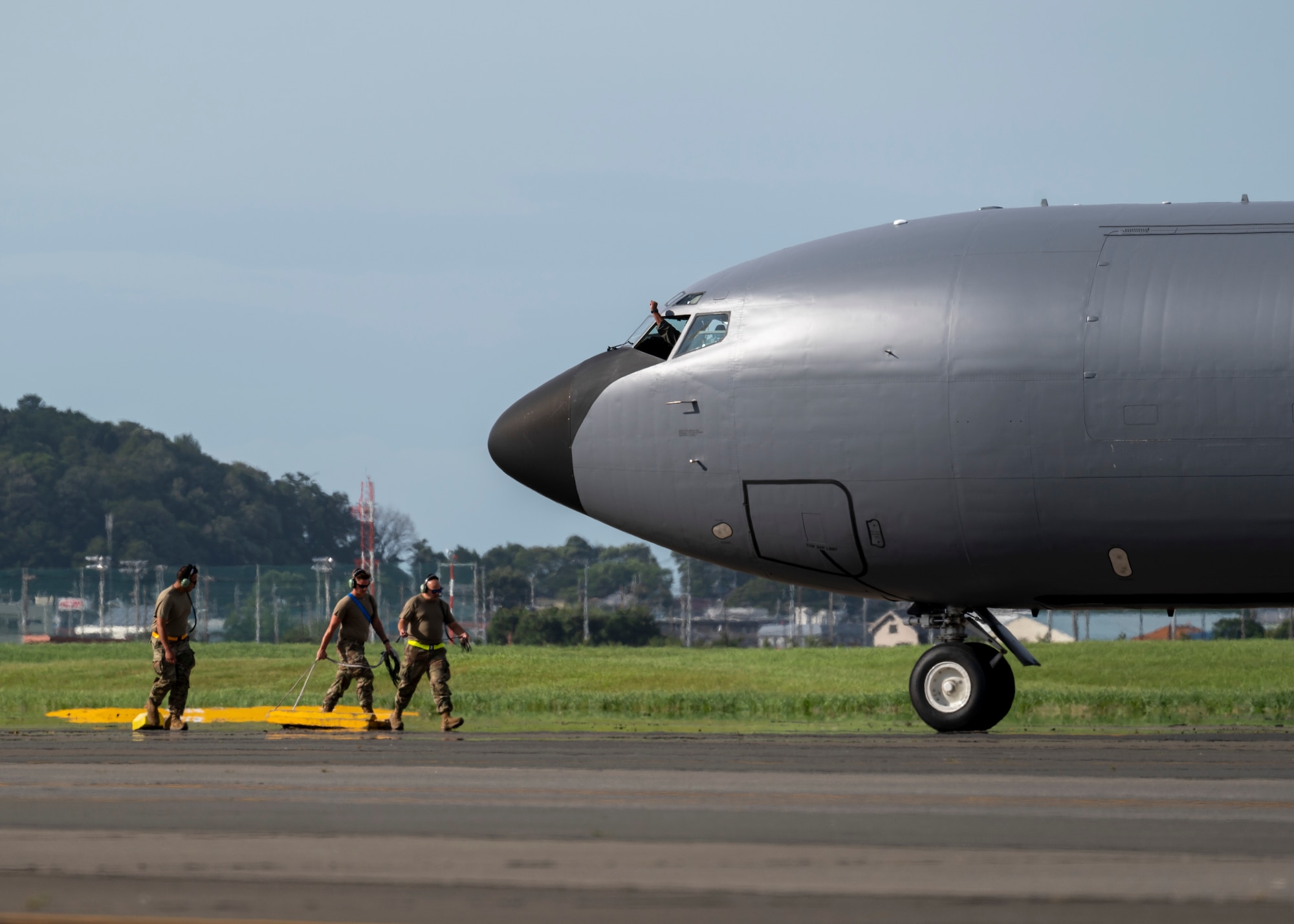 Three military members walk towards a parked KC-135 Stratotanker aircraft.