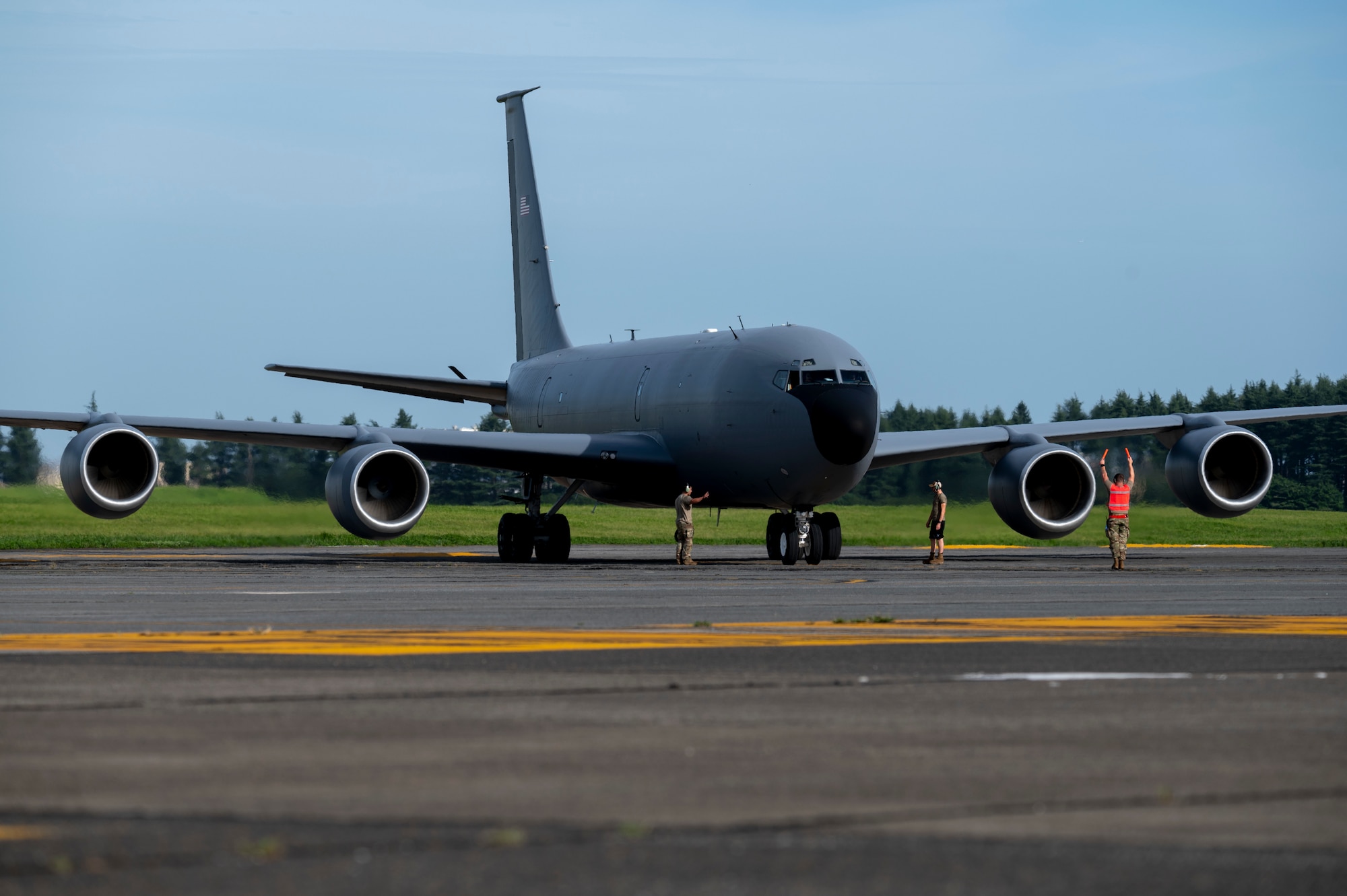 Military members stand in front of a KC-135 Stratotanker as it parks on the flightline.