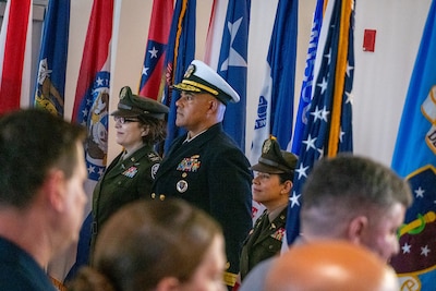 Photo of leaders participating in Transfer of Directorship ceremony from left to right, Col. Gina Adam, Rear Adm. Reginald Ewing, and Col. Elba Villacorta, standing at attention in front of flags with crowd in the foreground.