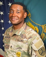Man in U.S. Army uniform standing in front of two flags.