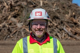 A photo of U.S. Army Corps of Engineers Quality Assurance inspector Ryan Williams at the Langsdale Temporary Debris Storage and Reduction site in Brooks County, Georgia on Feb. 21, 2025. He is stood in front of piles of debris cleaned up by USACE contractors following Hurricane Helene.