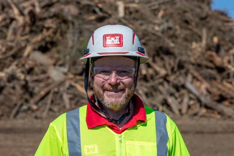 A photo of U.S. Army Corps of Engineers Quality Assurance inspector Ryan Williams at the Langsdale Temporary Debris Storage and Reduction site in Brooks County, Georgia on Feb. 21, 2025. He is stood in front of piles of debris cleaned up by USACE contractors following Hurricane Helene.
