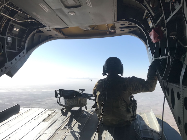 A U.S. soldier mans a rear-mounted gun while looking out the back ramp of a Chinook helicopter en-route to a remote base in central Afghanistan, part of a mission-critical deployment in support of base infrastructure. The flight carried a four-person technical team, including U.S. Army Corps of Engineers civilian contracting officer technical representative, Ryan Williams, tasked with replacing failed sewage lift pumps under armed escort beyond the base perimeter. (U.S. Army Photo by Ryan Williams)