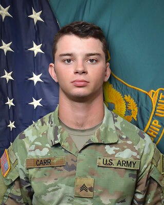 Man in U.S. Army uniform standing in front of two flags.