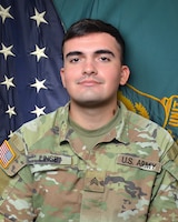 Man in U.S. Army uniform standing in front of two flags.