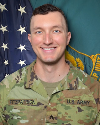 Man in U.S. Army uniform standing in front of two flags.